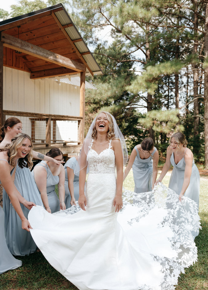 Bride laughing as bridesmaids fan out her dress